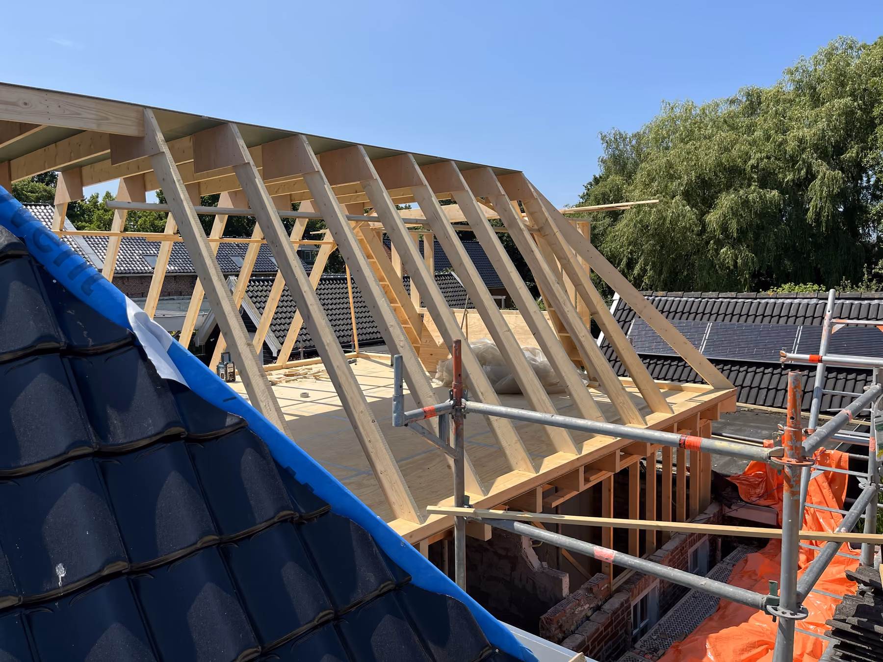 Nieuwe houten dakconstructie met sporen en gordingen tegen een blauwe lucht